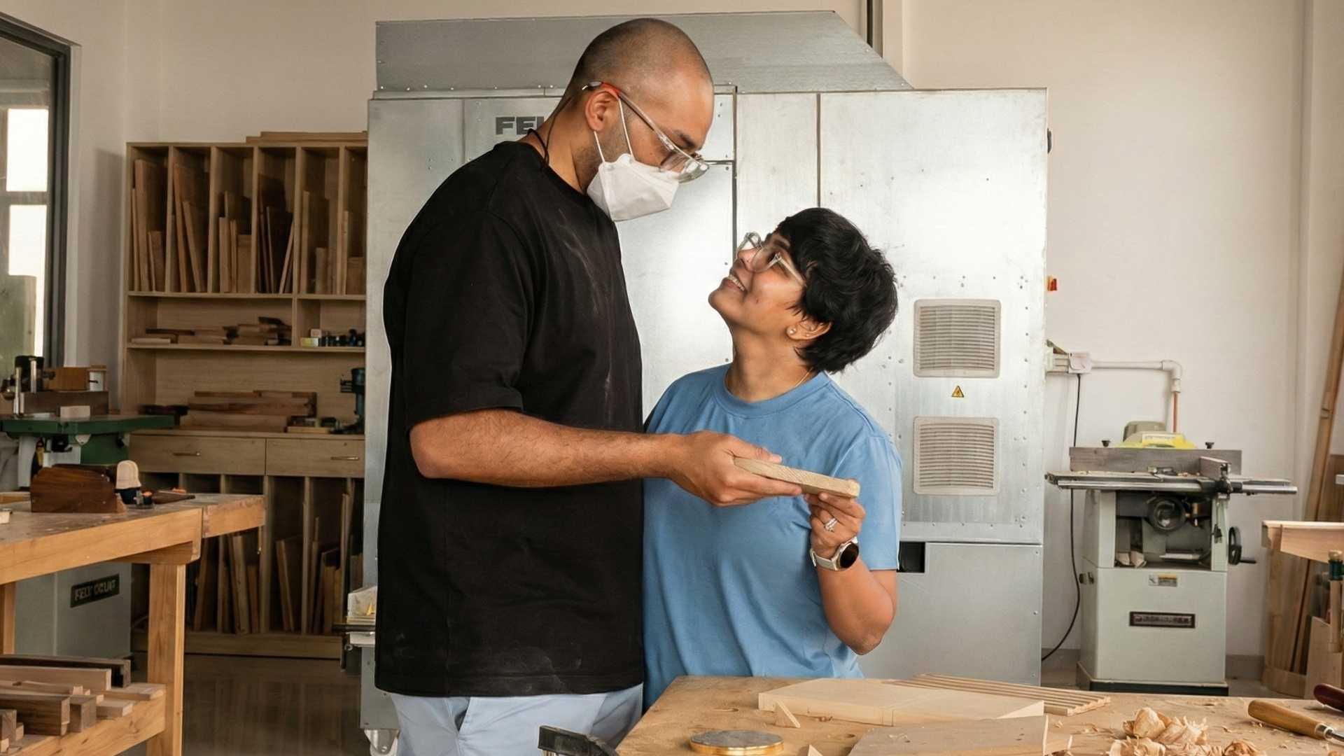 Couple sharing a woodworking moment in a Dubai workshop surrounded by tools and wood pieces