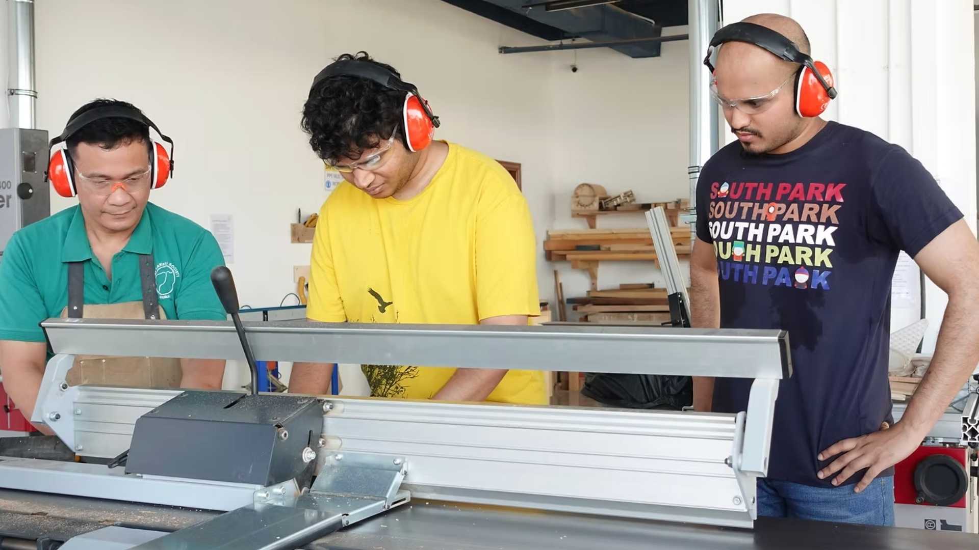Woodworking instructor demonstrating proper measuring and setup at jointer while students observe.