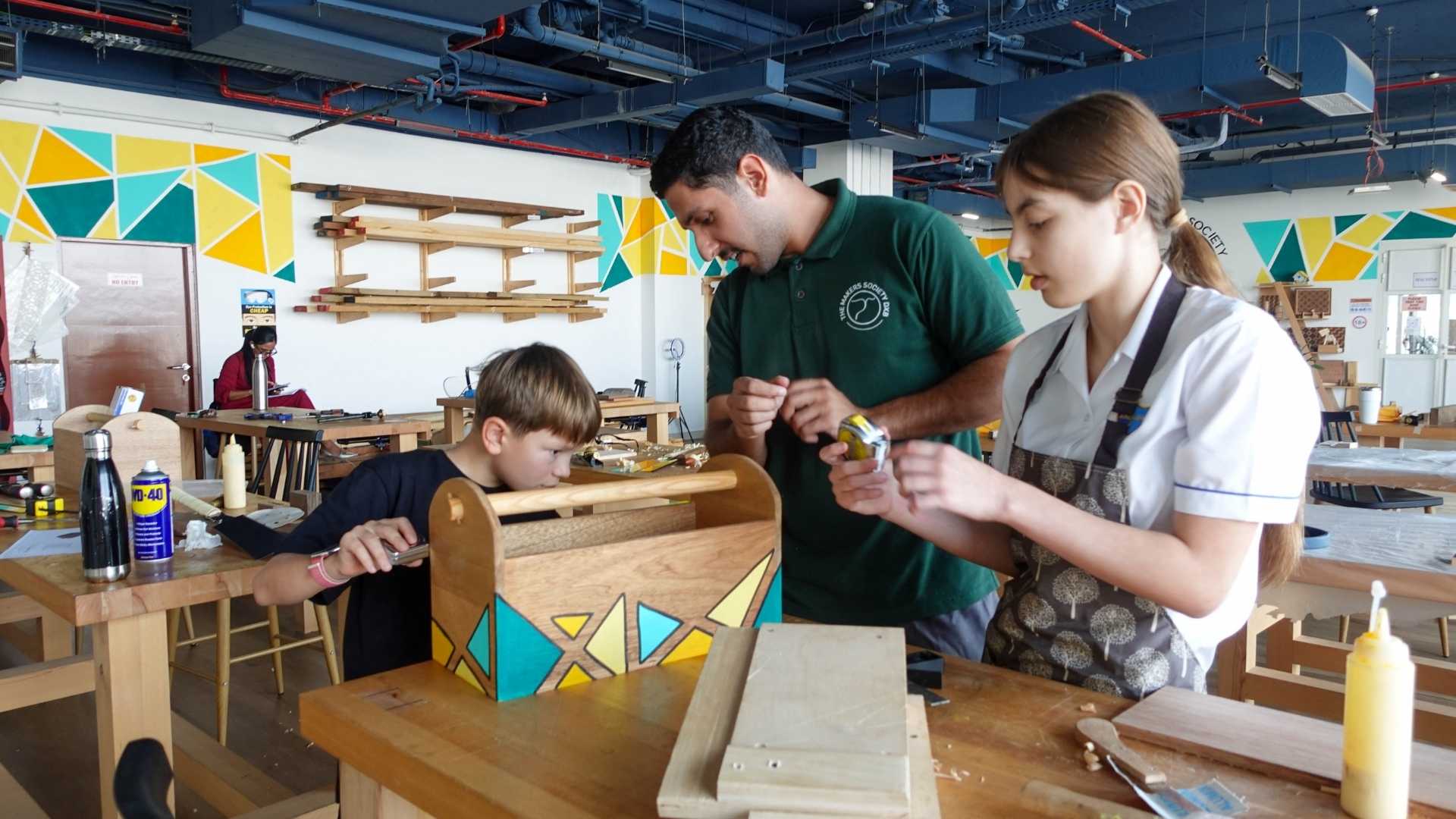 TMS instructor guiding school students at a woodworking bench in Dubai