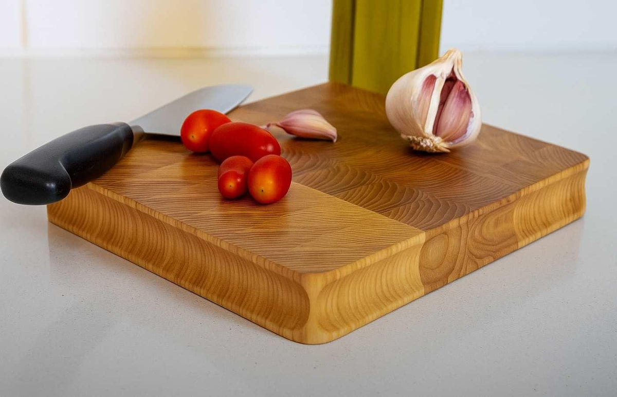 Premium wooden cutting board with fresh tomatoes, garlic, and a kitchen knife on white countertop