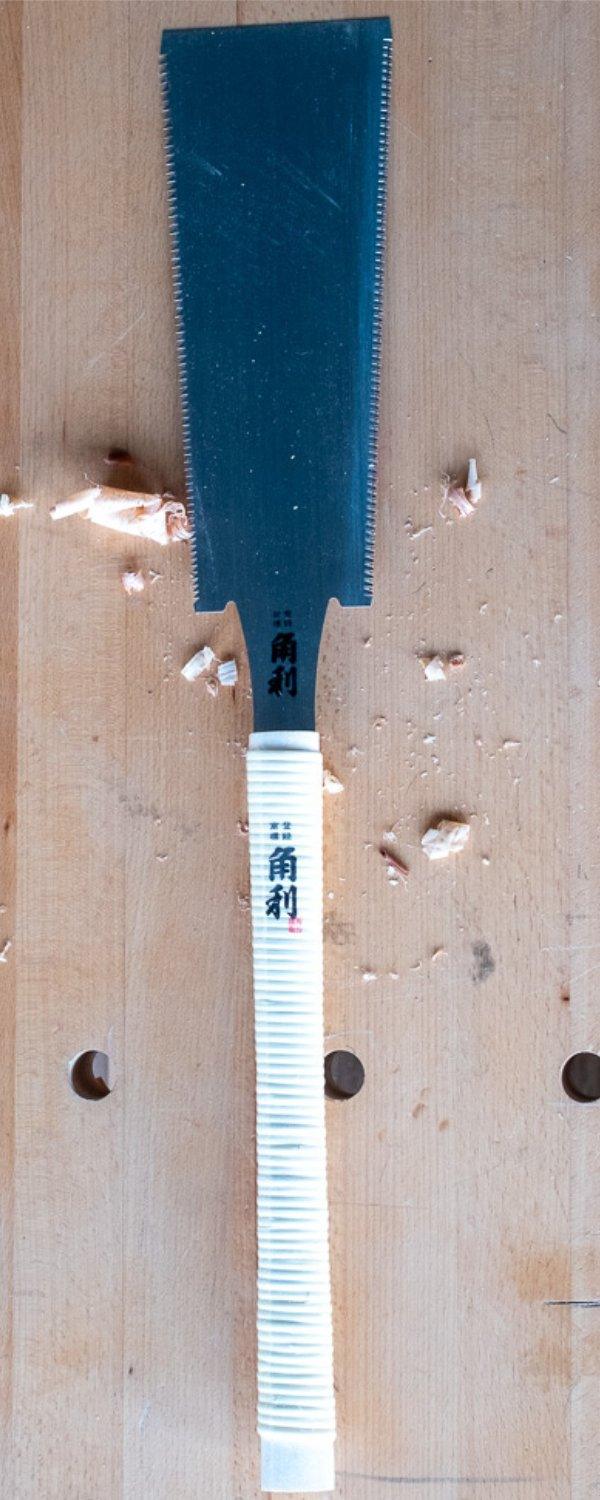 Japanese saw with white wrapped handle and fine teeth on a wooden surface with wood shavings