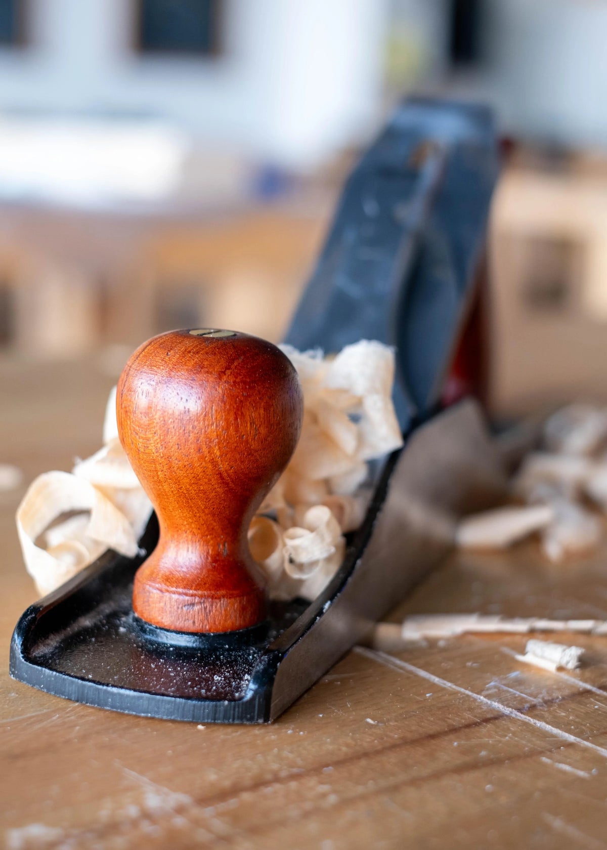 Close-up of a Luban 5 woodworking bench plane with wooden handle and wood shavings on a workshop table