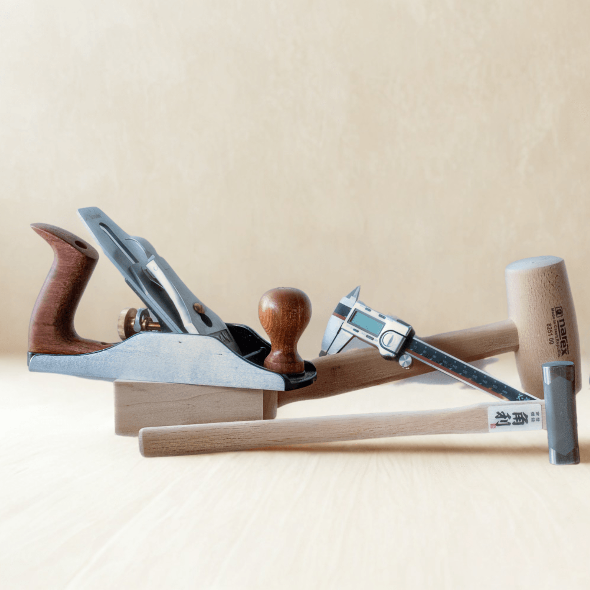 Set of woodworking hand tools including a hand plane, digital caliper, wooden mallet, and hammer on a light wood surface
