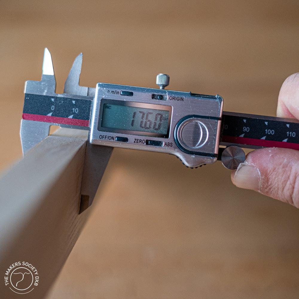 Hand using Absolute Zero digital caliper to measure 17.60 mm thickness of wooden board in woodworking setting