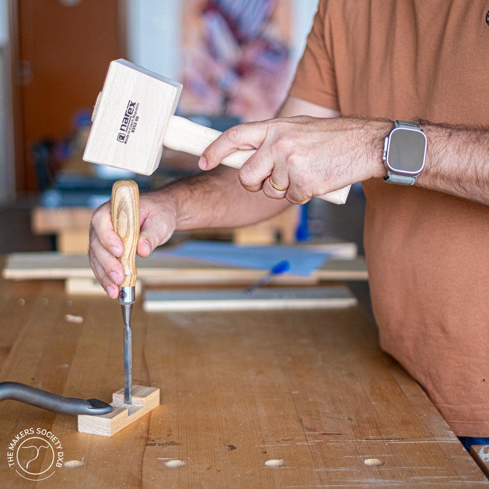 Woodworker using a Narex wooden mallet and chisel on a piece of wood in a workshop