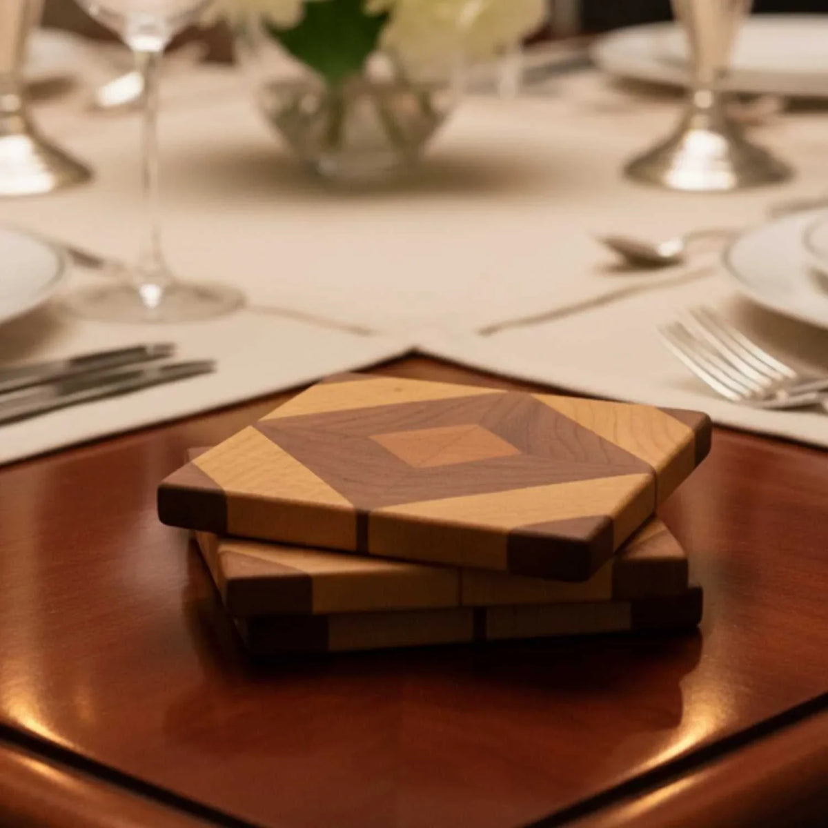 Set of two handmade wooden diamond-patterned coasters on polished wood table with elegant dining setup