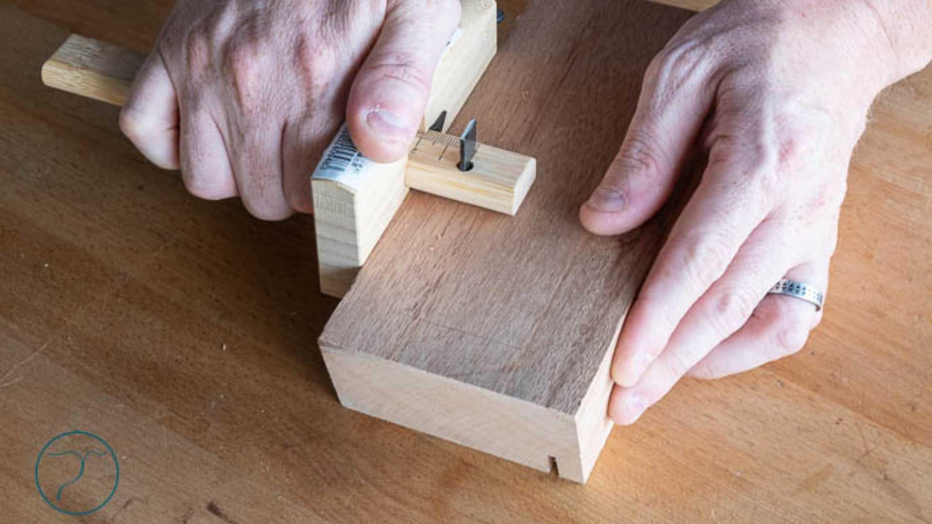 Hands using a Japanese Kakuri marking gauge on a wooden block for precise woodworking layout