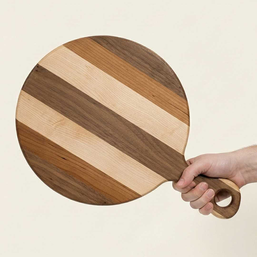 Hand holding a round striped wood serving board with handle, The Makers Society Shop