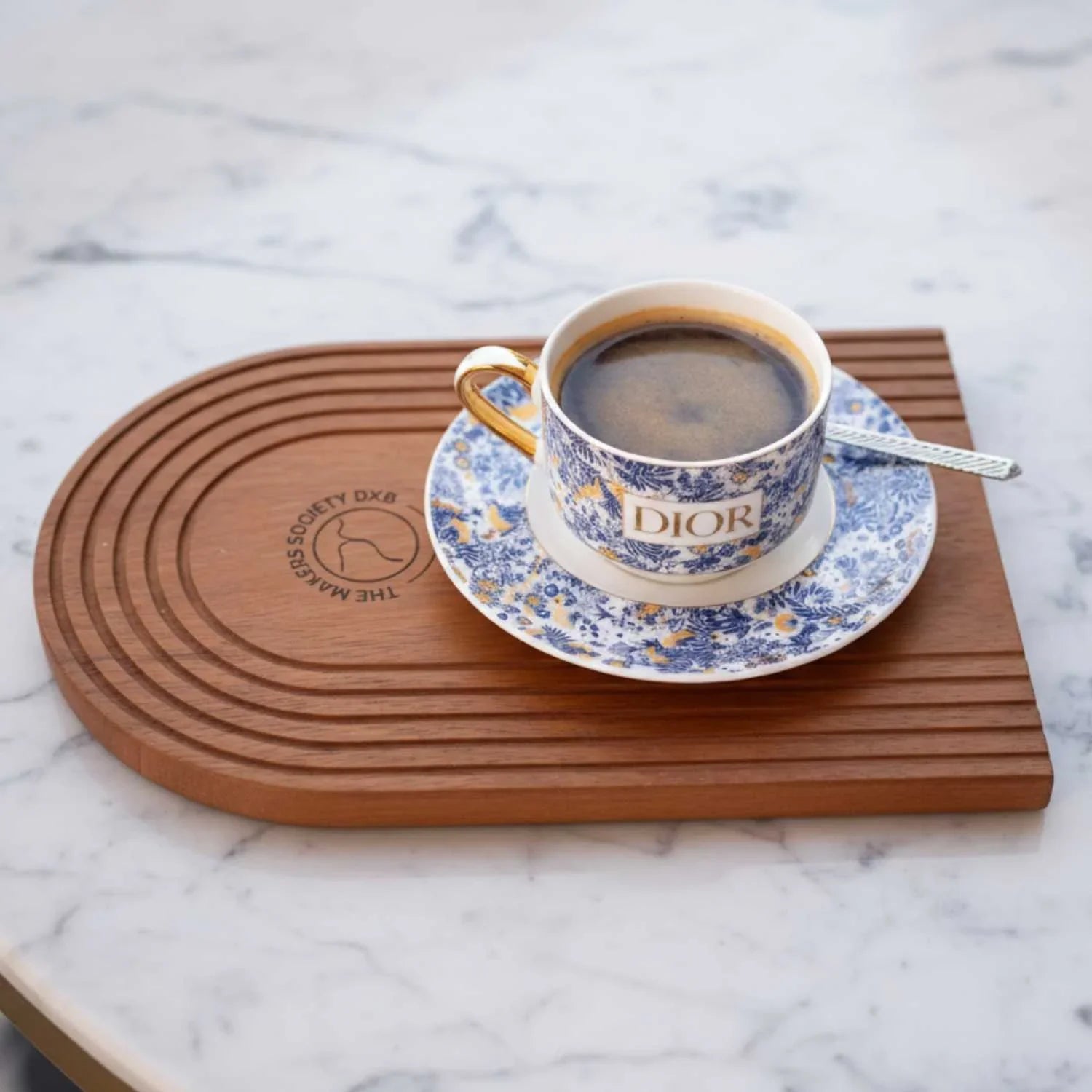 Grooved wooden serving tray from The Makers Society with a blue and white floral Dior coffee cup and saucer on marble surface