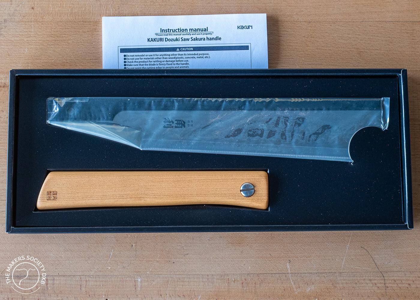 Kakuri Dozuki Saw with Sakura wood handle in black box packaging with instruction manual on wooden surface