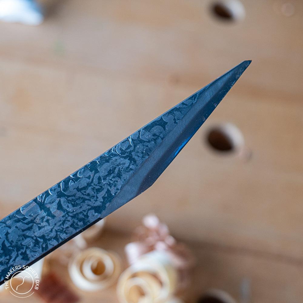 Close-up of a sharp Kakuri carving knife blade with textured blue steel, wood shavings background