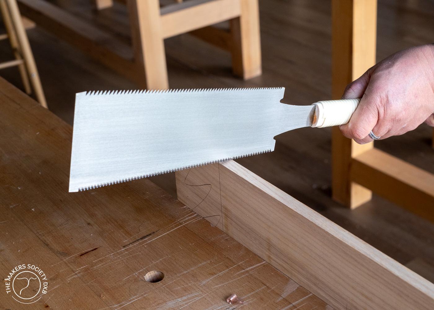 Hand holding a Kakuri Ryoba woodworking saw with a white handle cutting a dovetail joint on wood