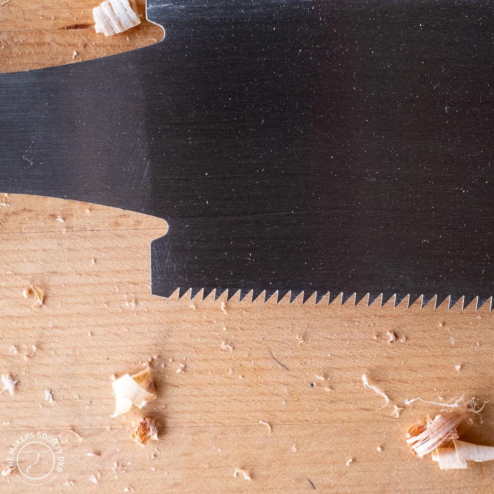 Close-up of Kakuri Ryoba woodworking saw blade with sharp teeth on wood surface with wood shavings