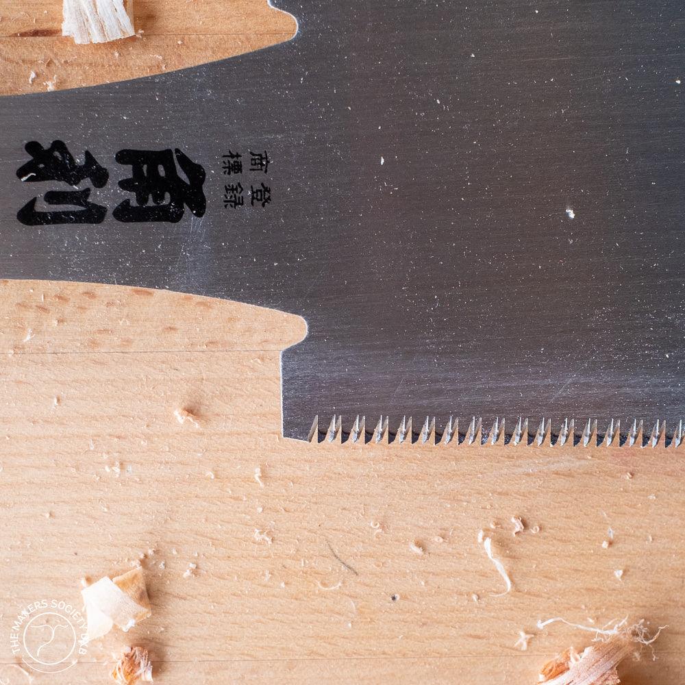 Close-up of a fine-tooth Japanese Ryoba saw blade with black kanji characters on wood surface with shavings