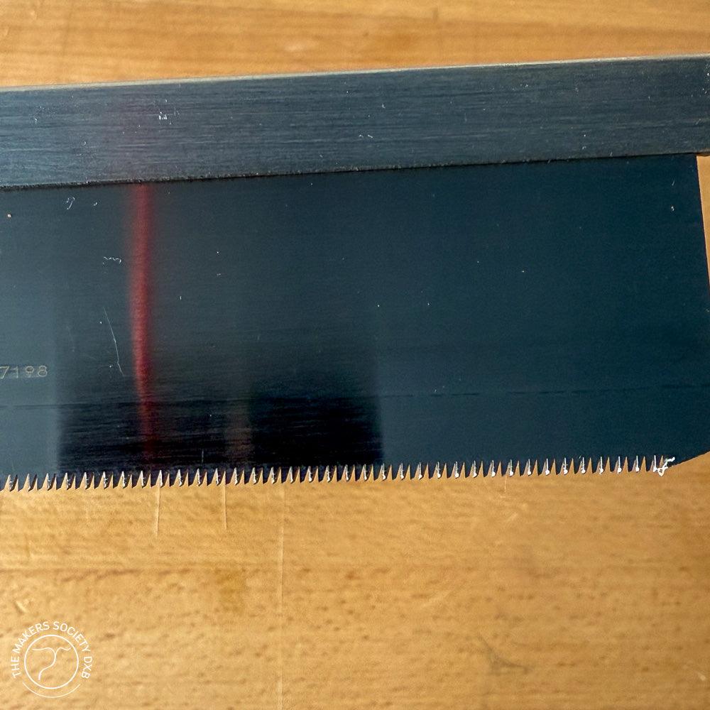 Close-up of 150mm Kakuri Dozuki woodworking saw blade with fine teeth on wooden surface