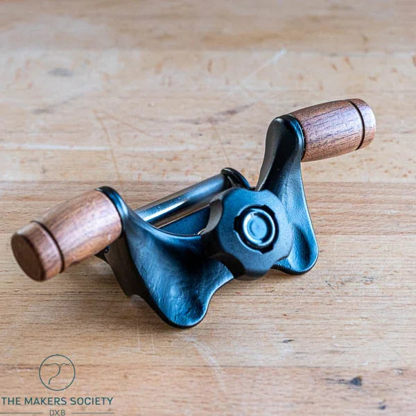 Honing guide with black metal body and wooden handles on wooden surface, woodworking tool by The Makers Society