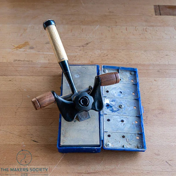 vintage woodworking honing guide with wooden handles on a wooden workbench and blue storage case