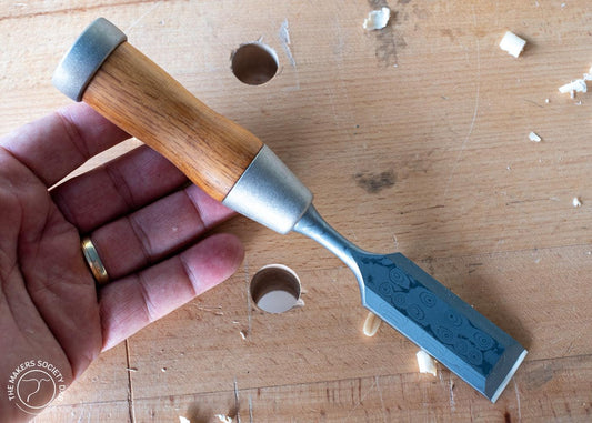 Hand holding a Kakuri highest grade Damascus steel woodworking chisel with wooden handle on a wood surface with wood shavings