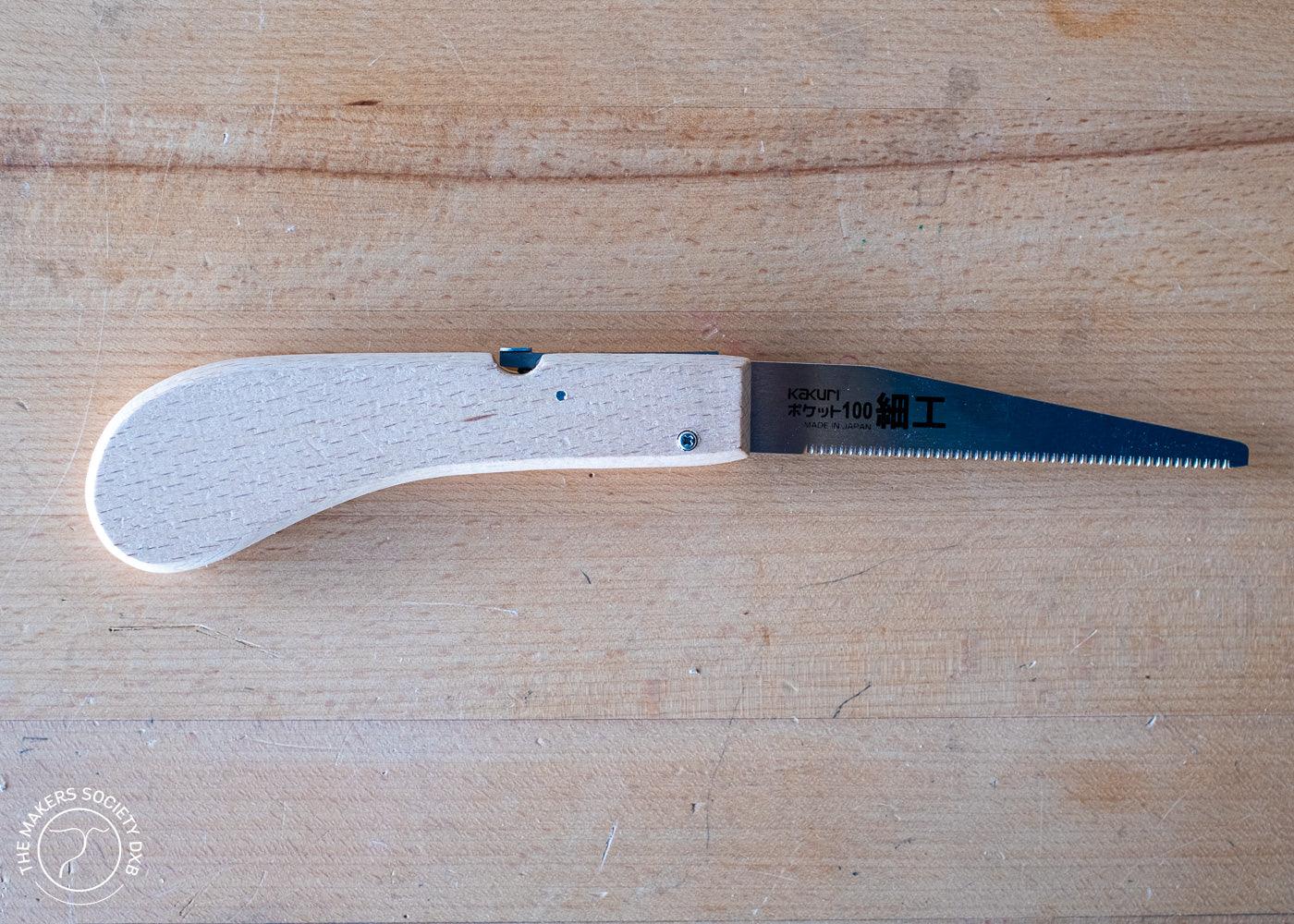 Kakuri Mini Folding Saw with wooden handle and sharp metal blade on wooden surface, precision woodworking tool