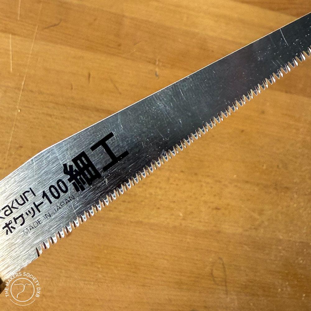 Close-up of Kakuri Mini Folding Saw blade with fine teeth on wooden background, made in Japan