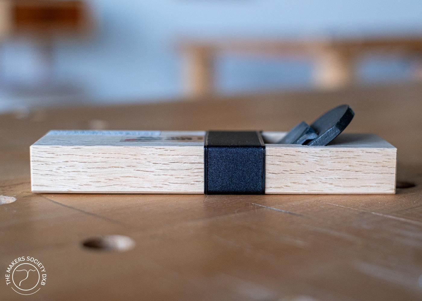 Kakuri mini hand plane with white oak body and black blade cap on wooden surface