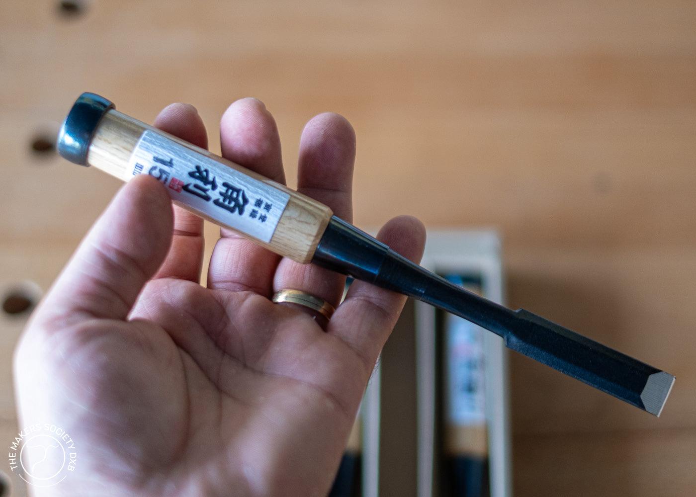 Hand holding a Japanese Kakuri Oire woodworking chisel with wooden handle and black metal blade