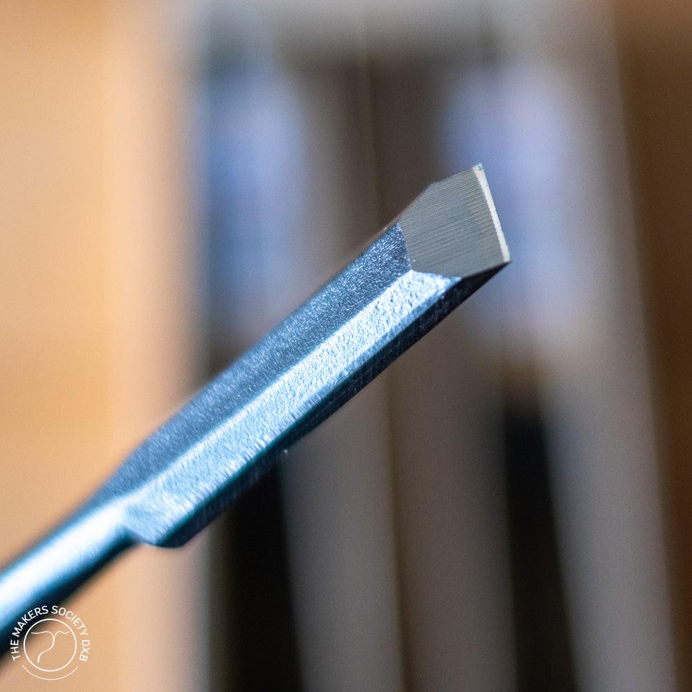 Close-up of a sharp metal woodworking chisel tip with textured handle in workshop setting
