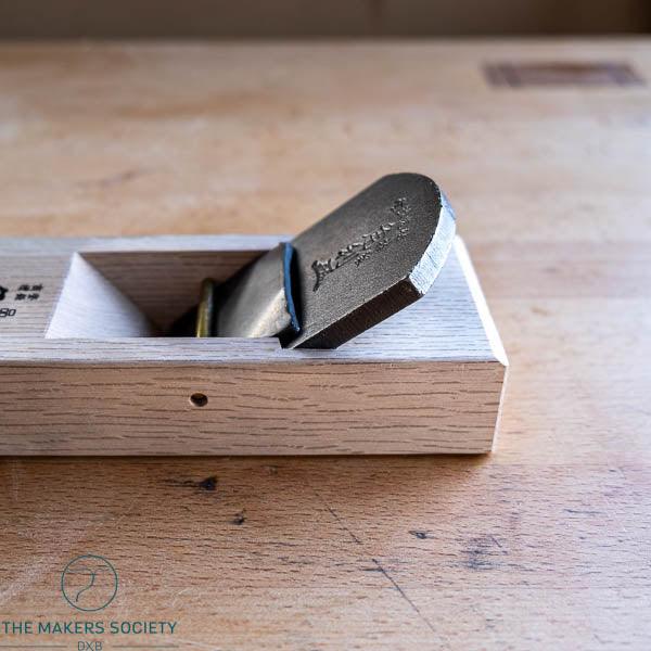 Smooth plane woodworking tool with white oak body and metal blade, placed on wooden workbench