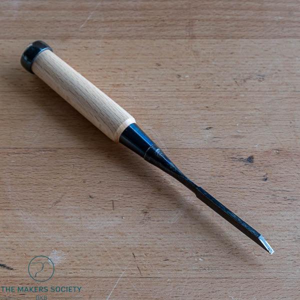 Wood chisel with a 3mm white steel blade and wooden handle on a wooden surface