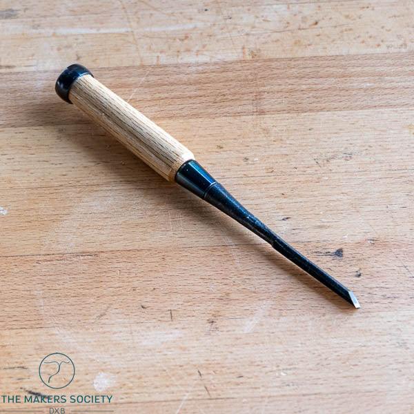 6mm wood chisel with white steel blade and wooden handle on a wooden surface