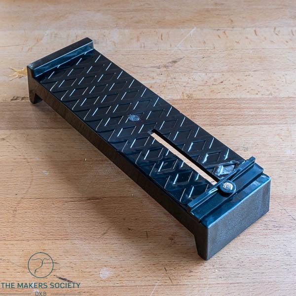 Black metal whetstone stand with adjustable slot on wooden surface, woodworking tool accessory