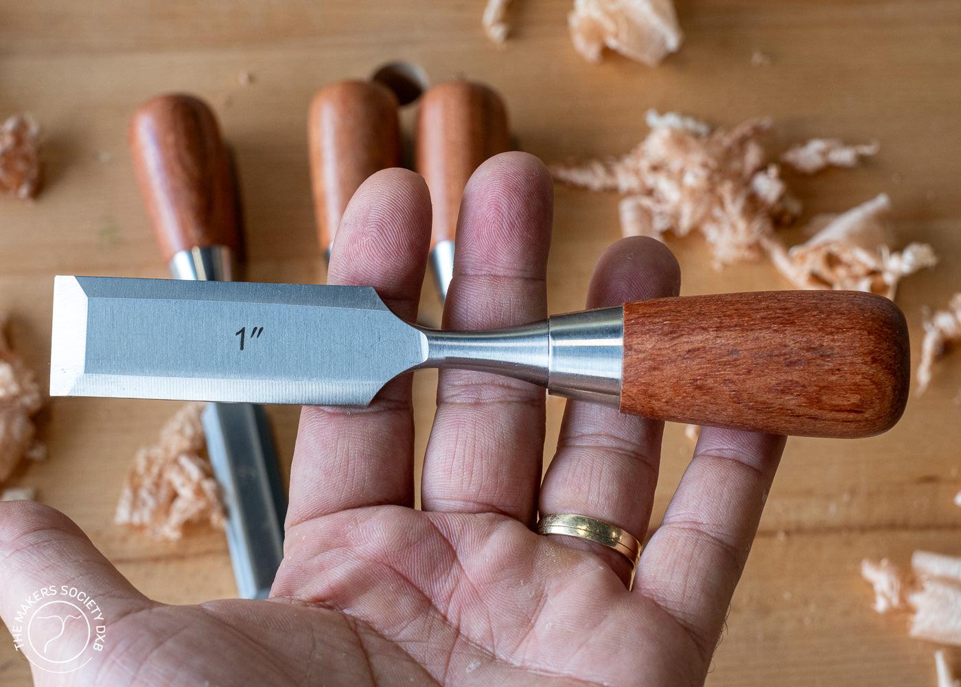 Hand holding 1-inch Luban butt chisel with wooden handle on woodworking surface with wood shavings