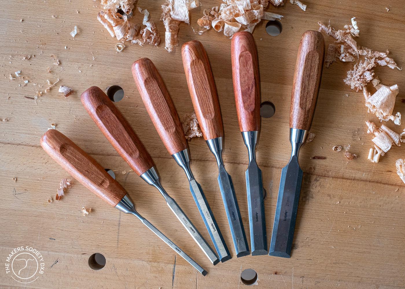 Set of six Luban woodworking bench chisels with polished wooden handles on a wooden surface with wood shavings