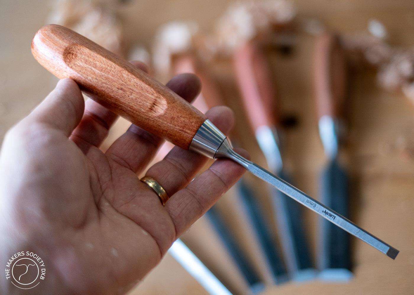 Hand holding a 6mm Luban bench chisel with wooden handle, other chisels blurred in background