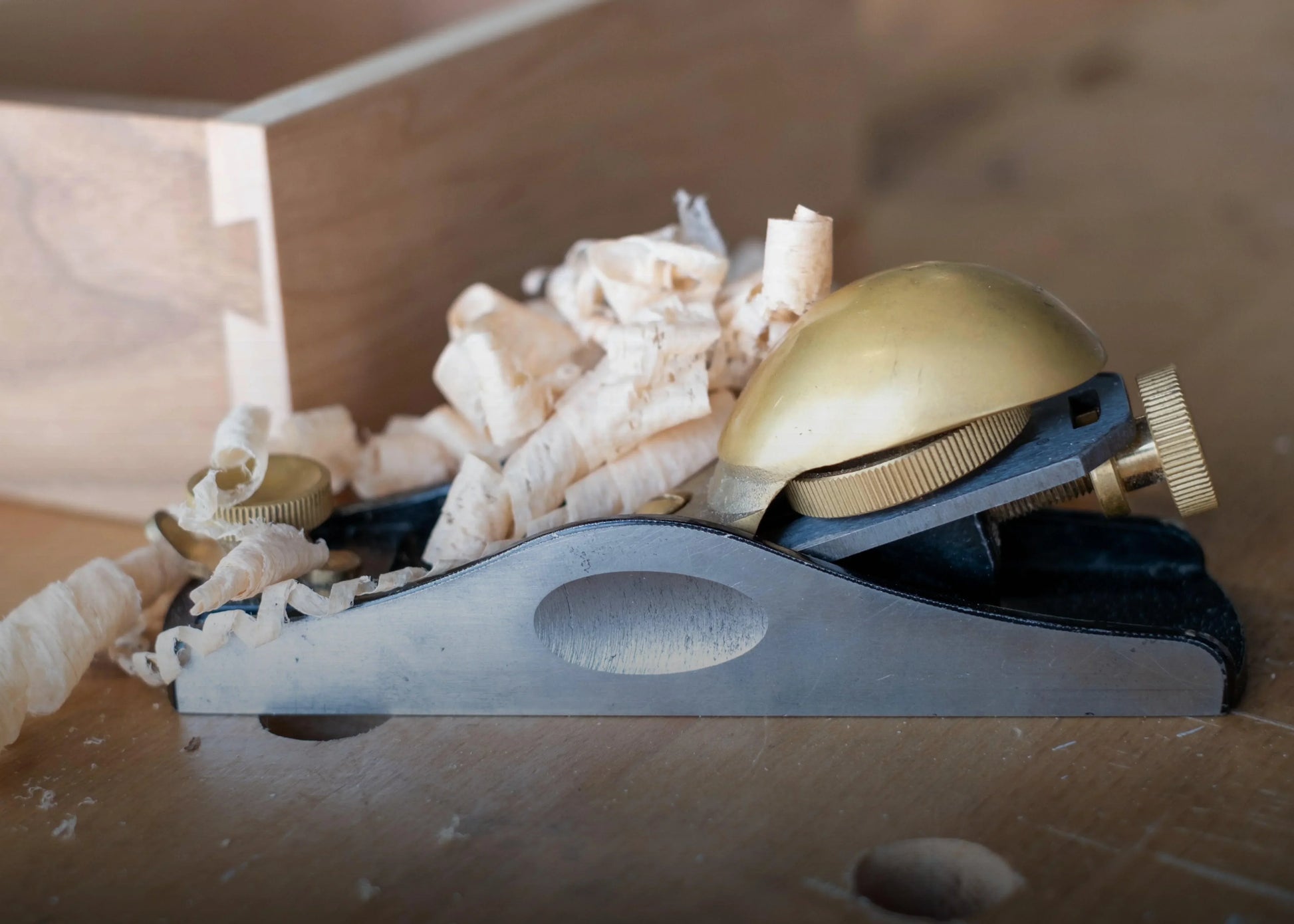 Close-up of a metal and brass woodworking block plane with wood shavings on a wooden workbench