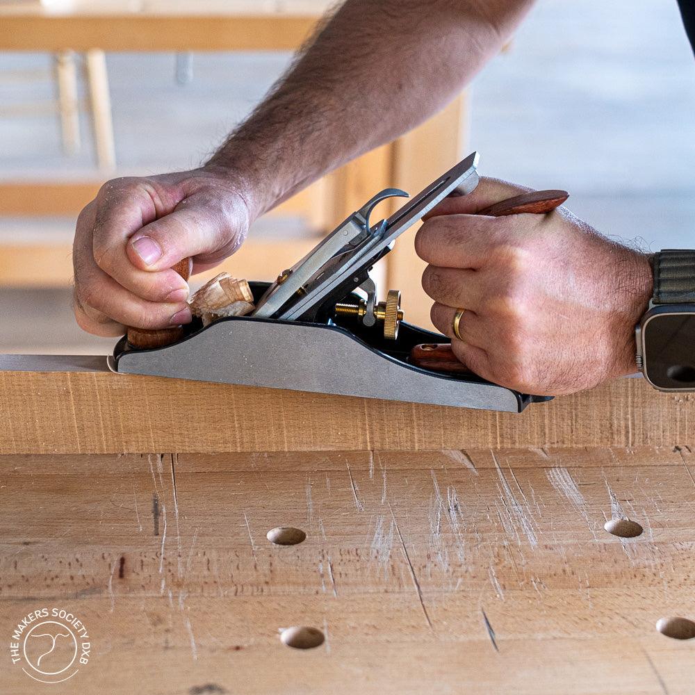 Close-up of hands using a bench plane on a wooden workbench in a woodworking workshop