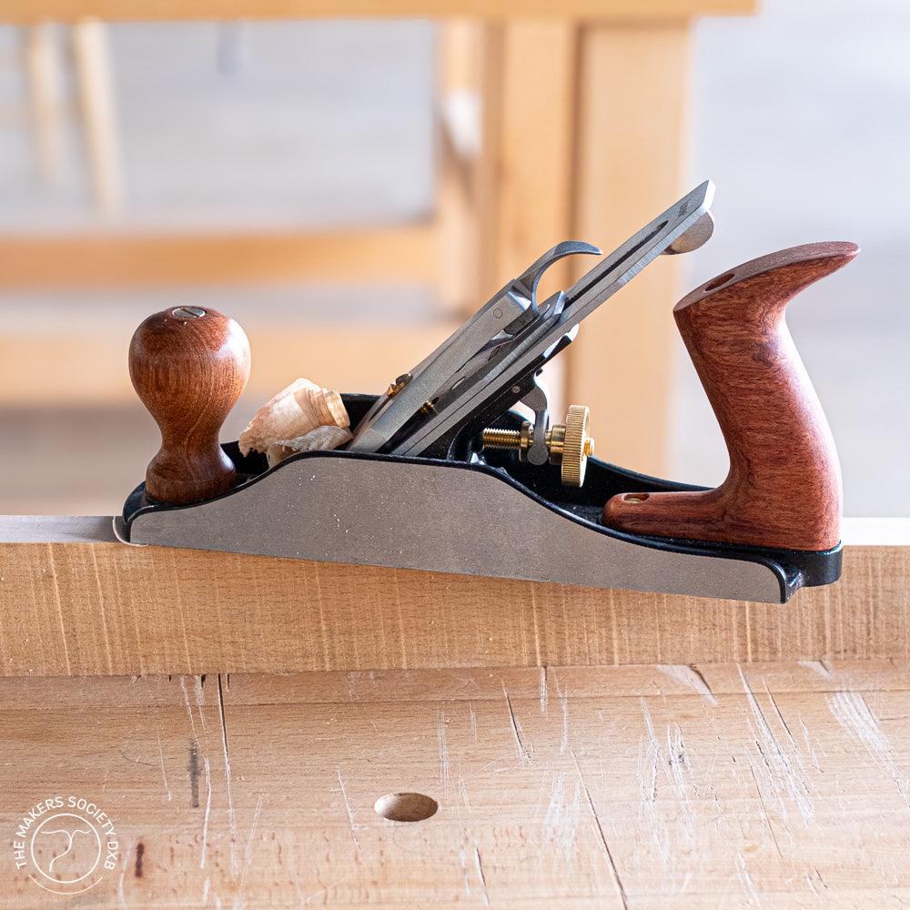 Luban bench plane with wooden handles on a woodworking bench, producing fine wood shavings