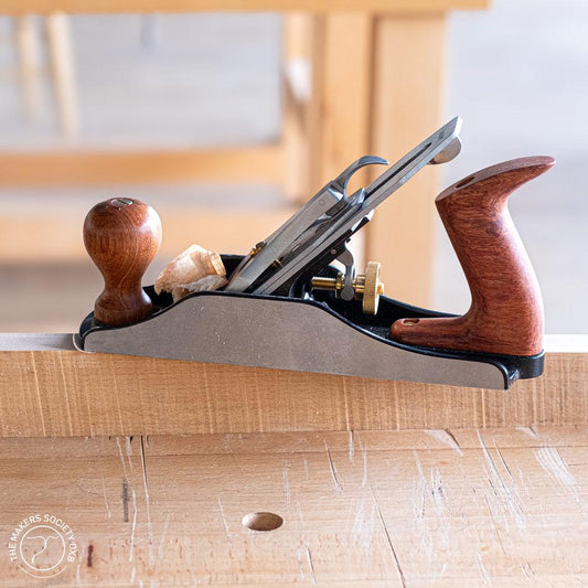 Luban bench plane with wooden handles on a woodworking bench, producing fine wood shavings