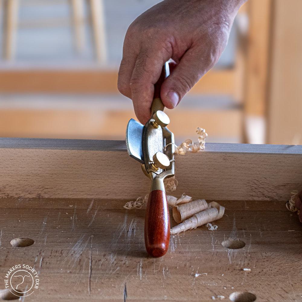 Hand using Luban Bronze spokeshave woodworking tool to shave wood curls on workbench