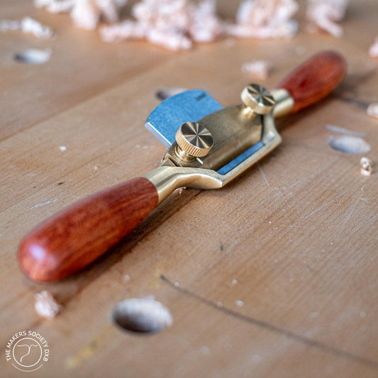 Bronze spokeshave woodworking hand tool with wooden handles on wooden workbench with wood shavings