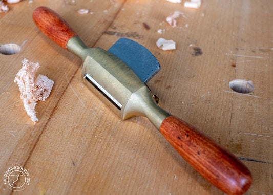 Luban bronze spokeshave with wooden handles on a woodworking bench with wood shavings