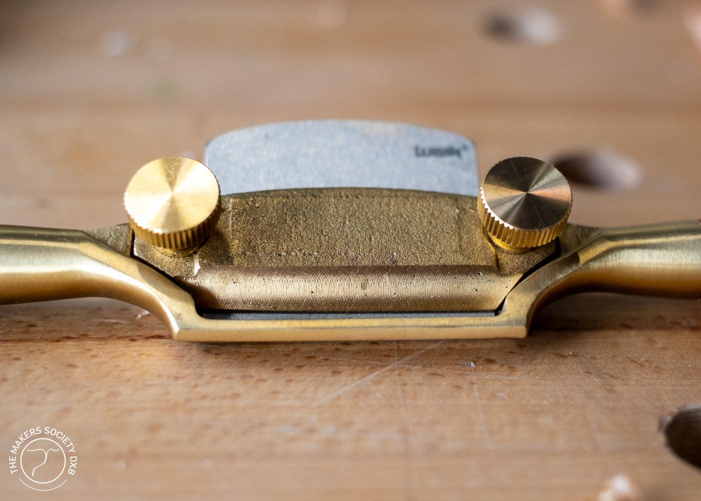 Close-up of a bronze Luban spokeshave woodworking tool with adjustable brass knobs on a wooden surface