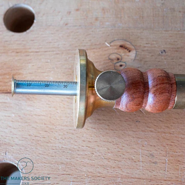 Close-up of Luban Marking Gauge with wooden handle and brass components on wooden surface at The Makers Society