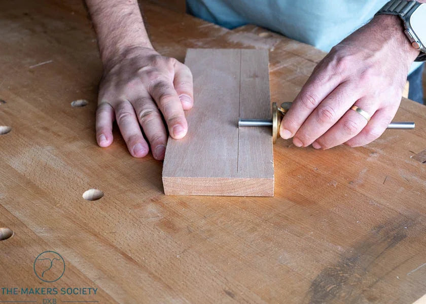 Hands using Luban marking gauge on wood plank on a woodworking bench from The Makers Society