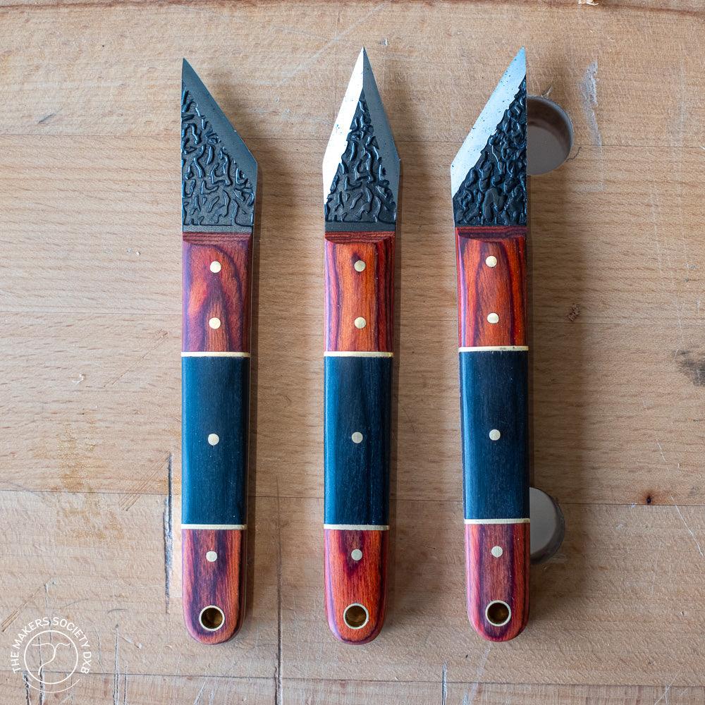 Set of three Luban marking knives with textured black blades and wooden handles on a woodworking bench