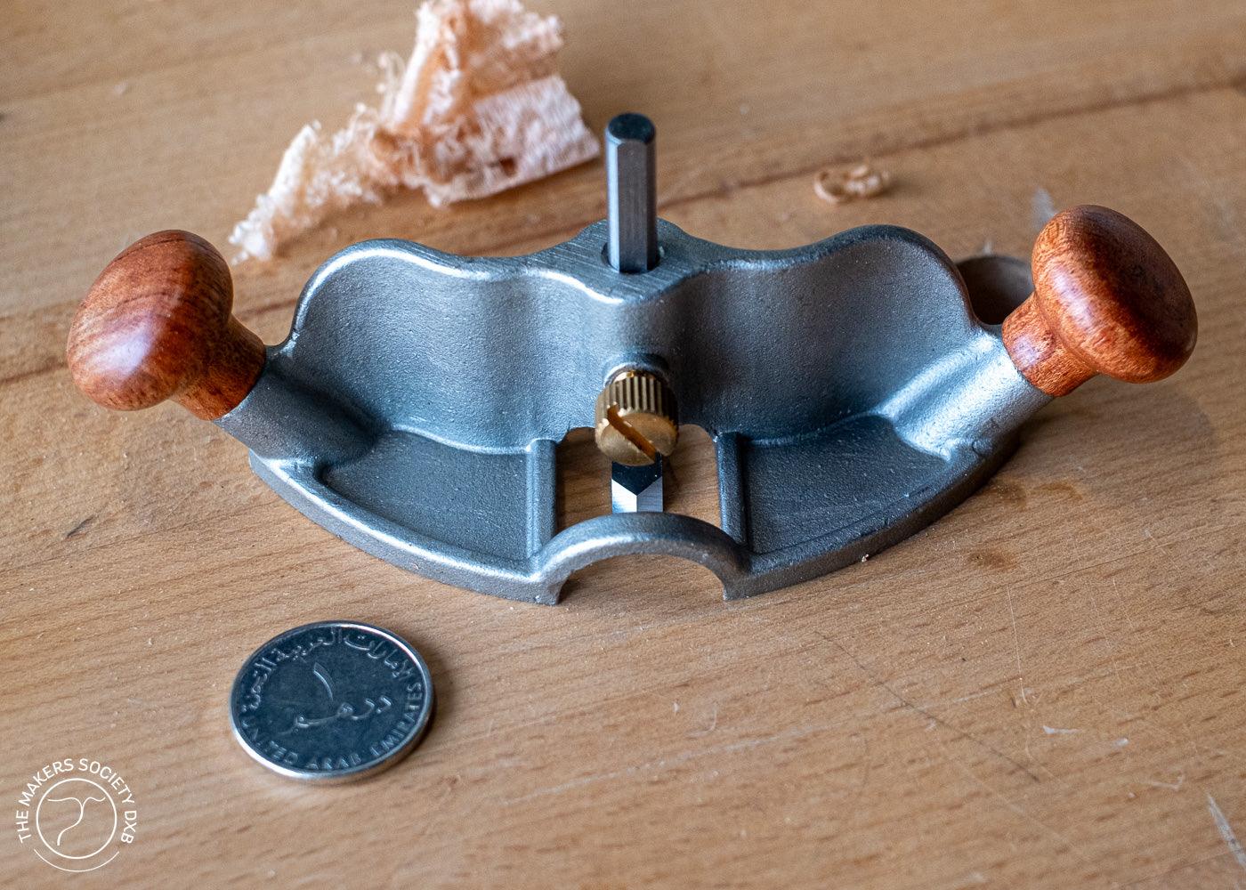 Luban router plane with wooden handles on woodworking bench next to UAE dirham coin and wood shavings