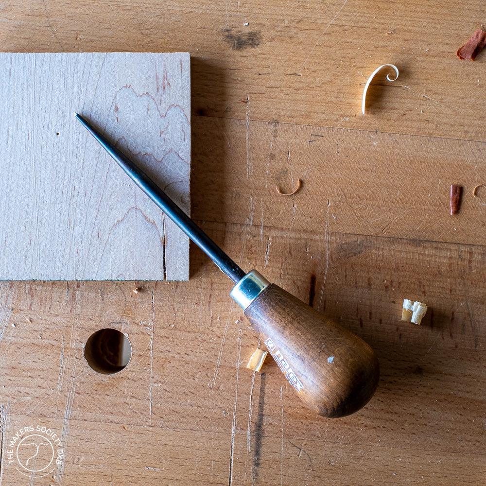 Narex conical woodworking awl with wooden handle on a workbench with wood shavings and a small wooden board