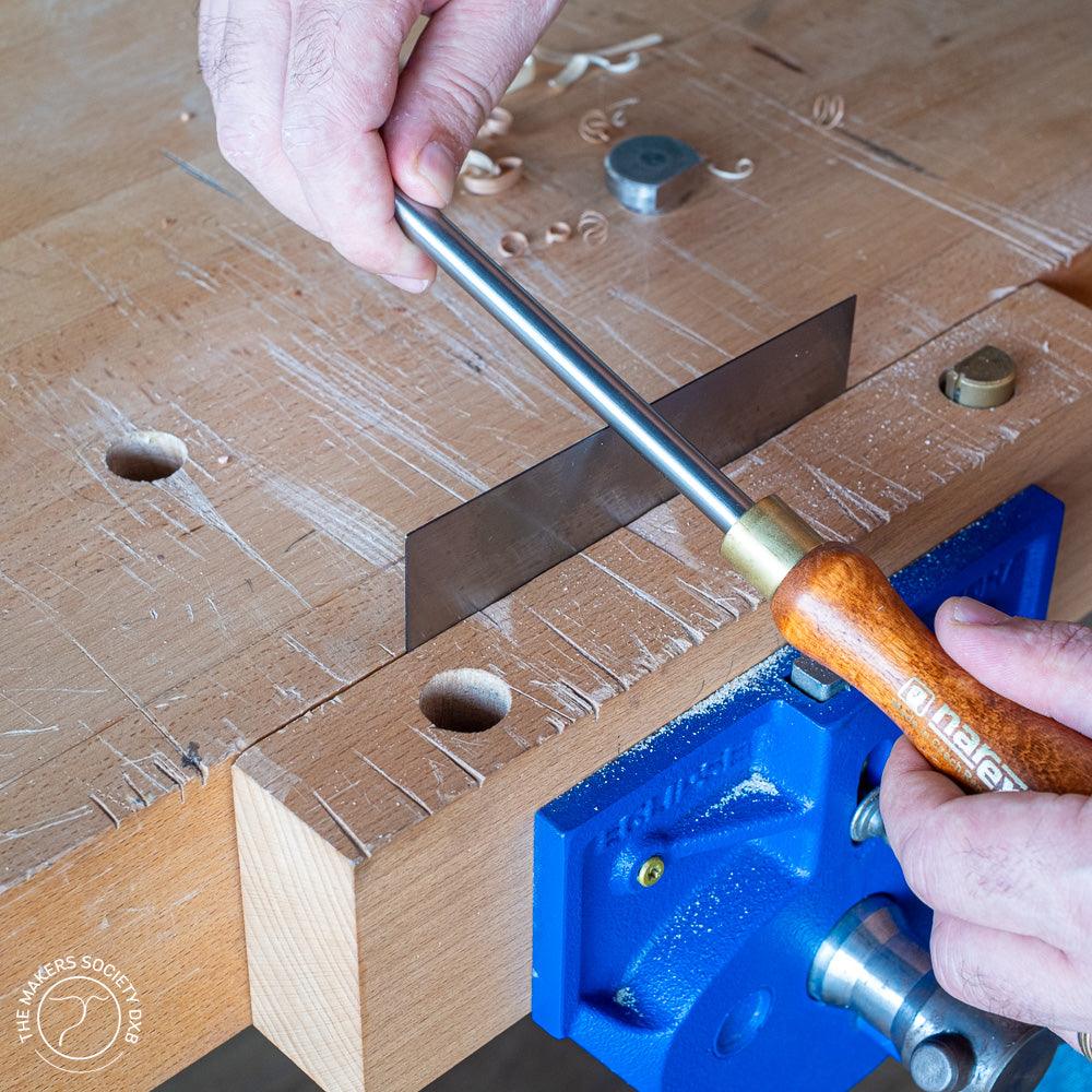 Hand using Narex burnisher tool with wooden handle on woodworking bench with blue vise and wood shavings