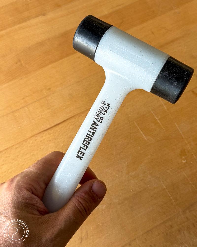 Hand holding a Narex antireflex mallet with black plastic faces and light blue handle on wooden surface