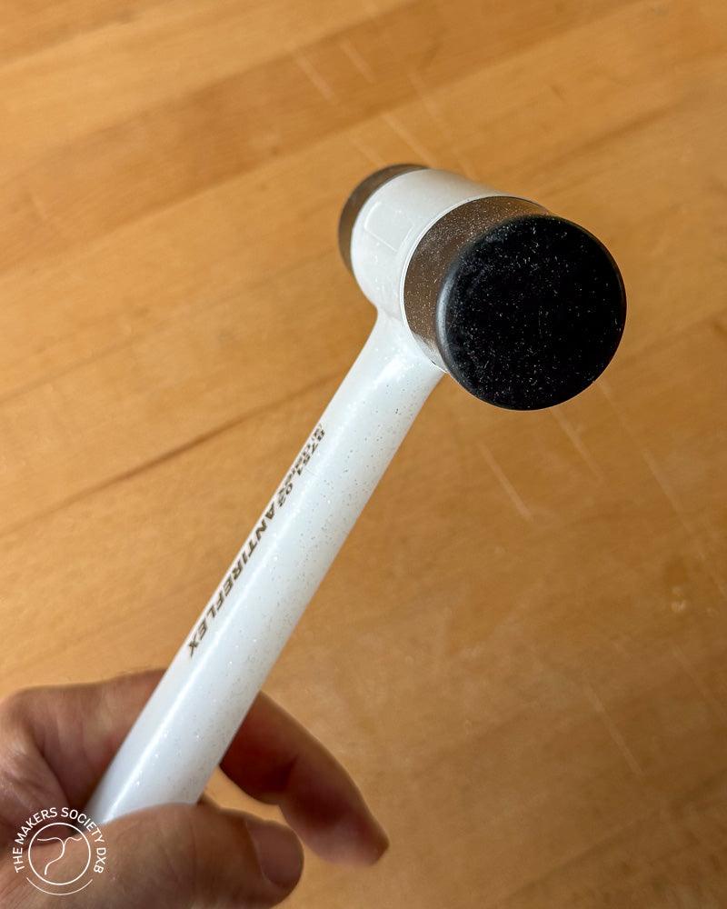 Close-up of a white Narex bounceless mallet with black plastic faces held over a wooden surface, woodworking tool